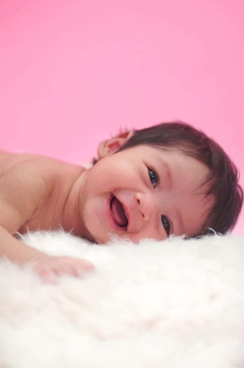 Foto newborn bayi tertawa di atas bulu putih, hasil sesi foto bayi Alfa Elfa Photography