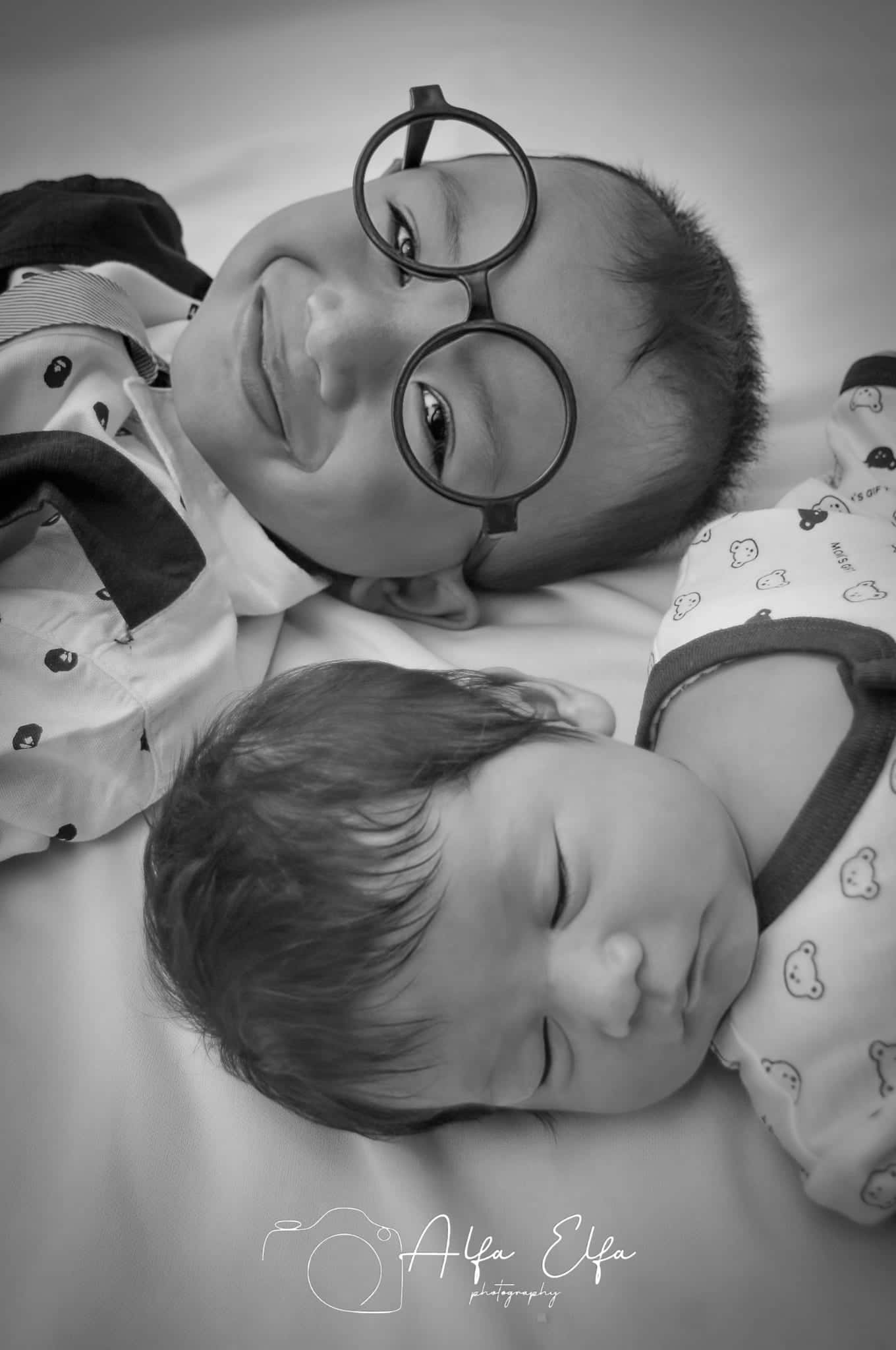 Foto newborn kreatif hitam putih dua bayi dengan properti kacamata