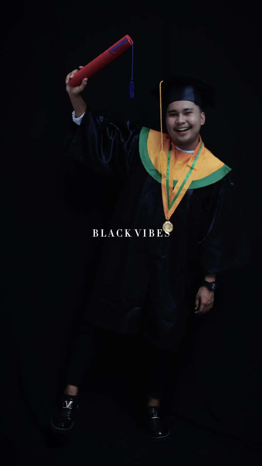 Foto wisuda pria toga dengan medali di depan backdrop hitam
