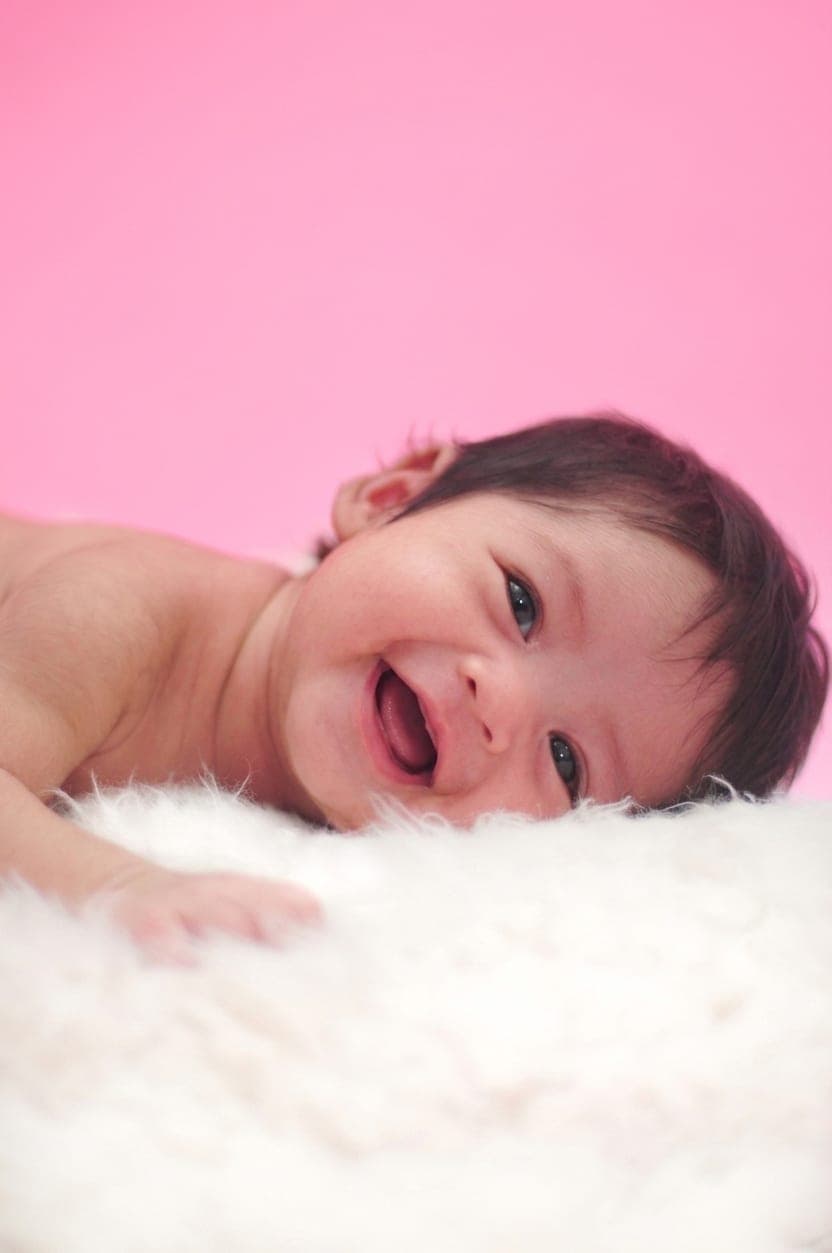 Foto newborn bayi tertawa di atas bulu putih, hasil sesi foto bayi Alfa Elfa Photography